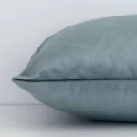 A solid-coloured sage green cushion cover is laid flat. This angle shows the side of the velvet fabric and its rectangular shape.