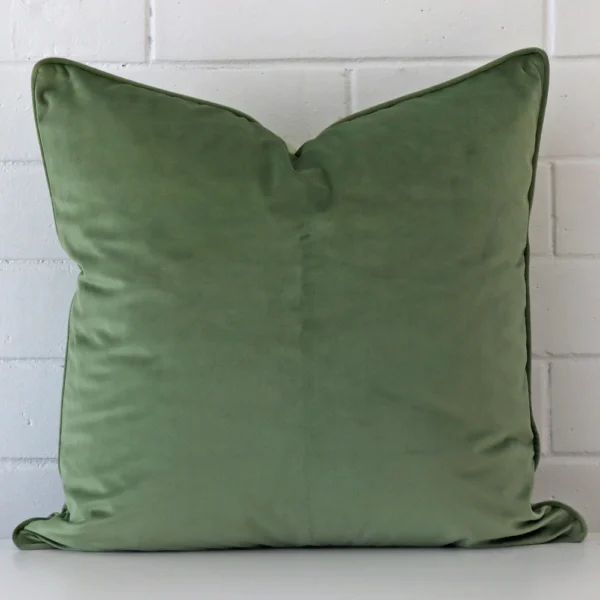 Sage cushion positioned in front of a brick wall. It has large dimensions and is made from a velvet material.
