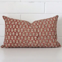 Floral cushion leans elegantly against a brick wall. It has been crafted from a high quality designer material and has a rectangle shape.