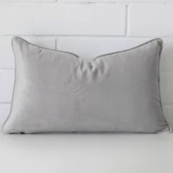 A pretty velvet cushion cover is shown against a brick wall. It features a rectangle shape and a silver grey colour finish.