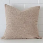 A pretty boucle cushion cover is shown against a brick wall. It features a large shape and a beige colour finish.