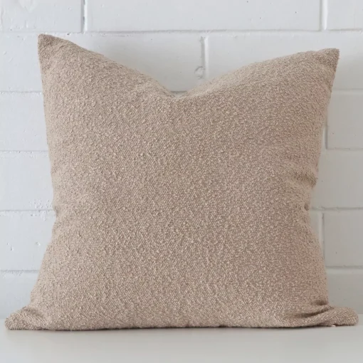 A pretty boucle cushion cover is shown against a brick wall. It features a large shape and a beige colour finish.