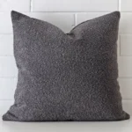 A lovely large dark grey cushion made from a boucle material cover arranged in front of a white wall.