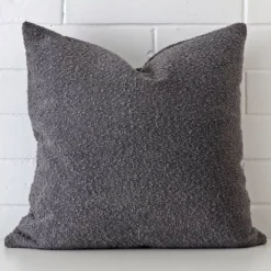 A lovely large dark grey cushion made from a boucle material cover arranged in front of a white wall.