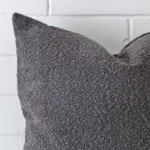 A zoomed in photo of the corner of a dark grey cushion that has boucle fabric and a large size.