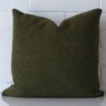 Olive green cushion positioned in front of a brick wall. It has large dimensions and is made from a boucle material.