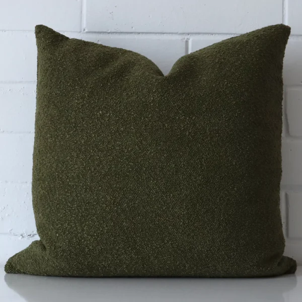 Olive green cushion positioned in front of a brick wall. It has large dimensions and is made from a boucle material.