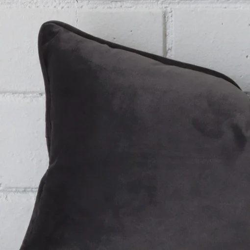 Enlarged shot of the corner of this rectangle cushion cover in space grey colour is shown against a brick wall. The image shows the quality and craftsmanship of the velvet material.