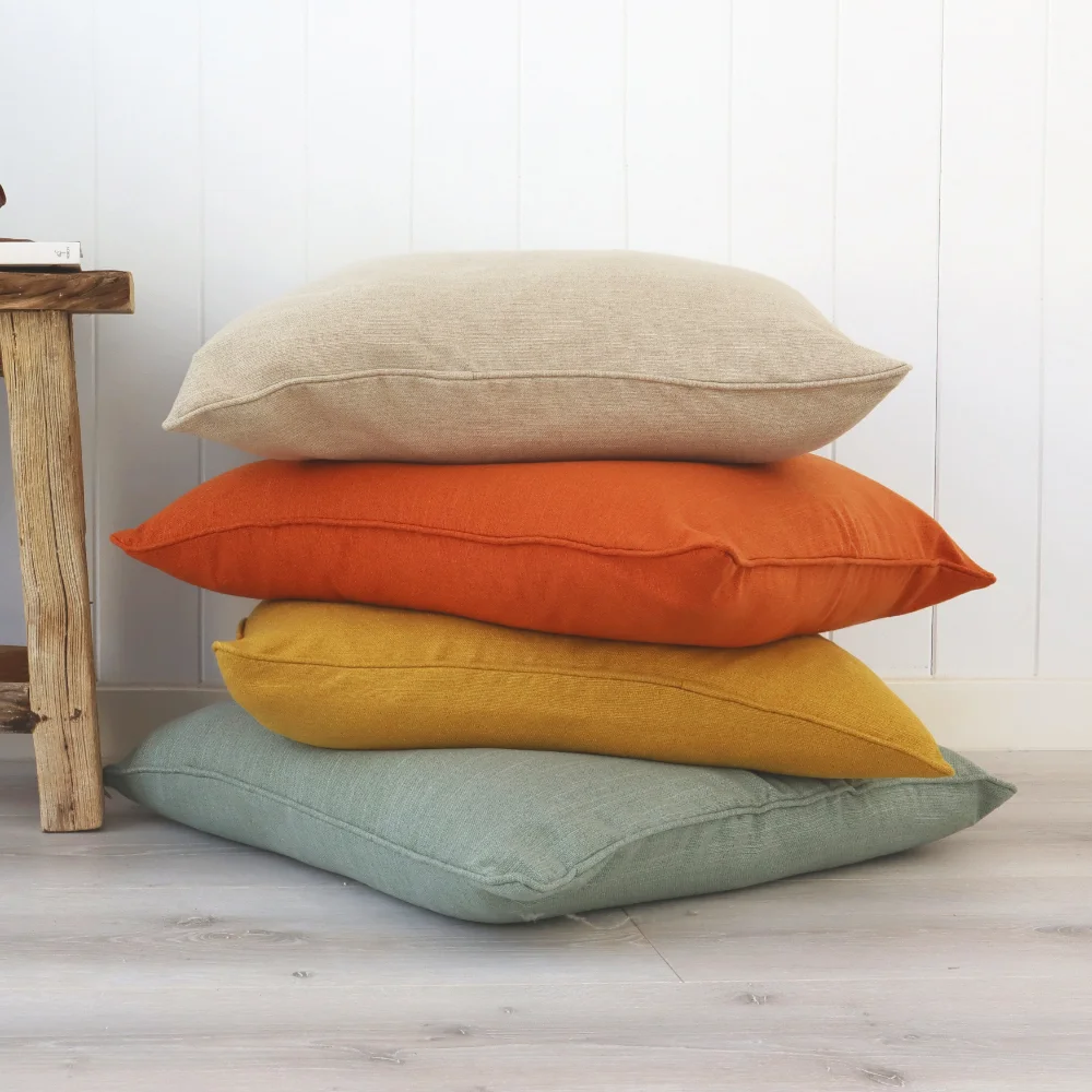 A stack of premium plain cushions sit on the floor of a room.