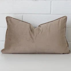 A lovely rectangle taupe cushion cover arranged in front of a white wall. It has a soft velvet material.