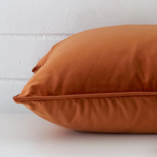 Horizontal edge of large cushion cover is shown. The velvet fabric and terracotta tone can be seen from this side view.