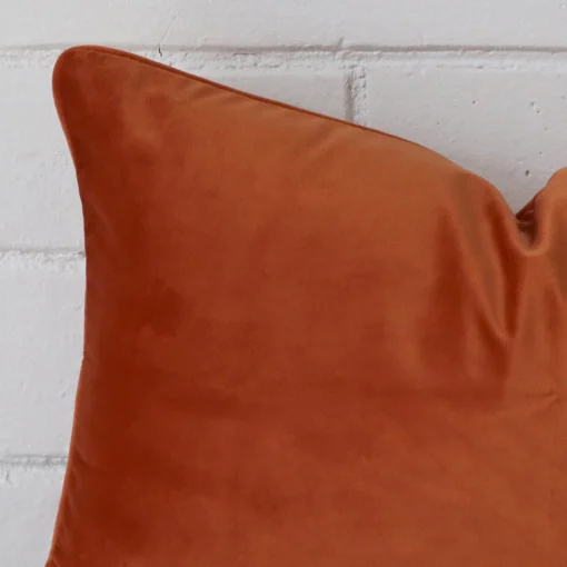 A zoomed in photo of the corner of a terracotta cushion that has velvet fabric and a rectangle size.