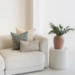A sofa next to a plant displaying 3 designer covers from the Vada set.