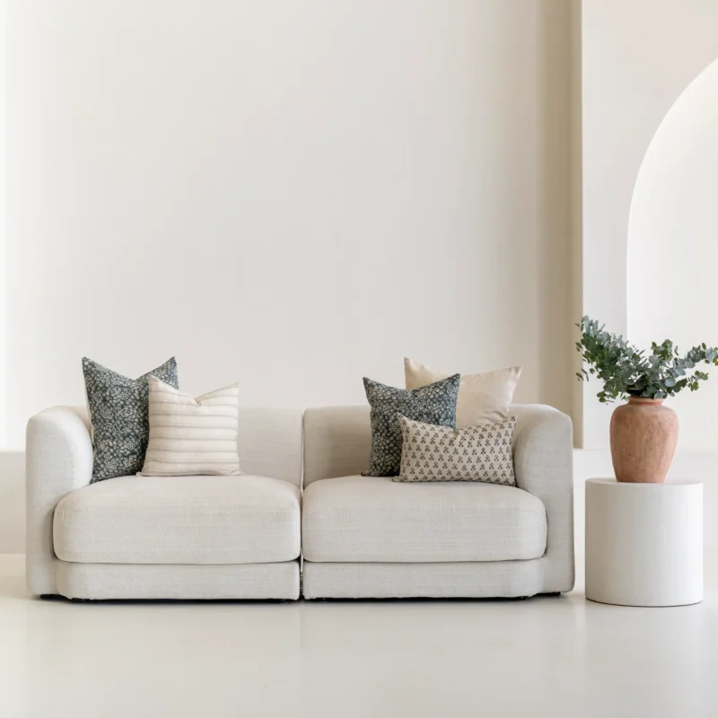 A living room featuring a natural-coloured sofa adorned with a neatly arranged set of 5 Vada designer cushion covers.