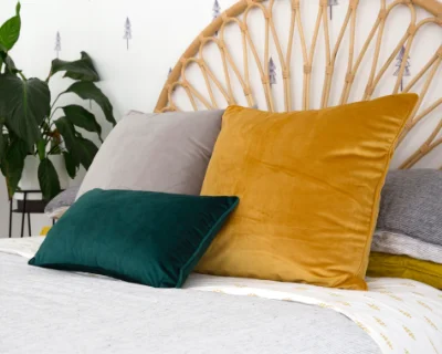 A collection of velvet cushion covers in grey, mustard and green arranged on a bed with a throw rug.