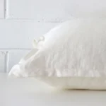 A white cushion arranged sideways in front of a wall. The large size and linen fabric are shown and the seams are clearly visible.