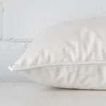 Horizontal edge of rectangle cushion cover is shown. The velvet fabric and white tone can be seen from this side view.