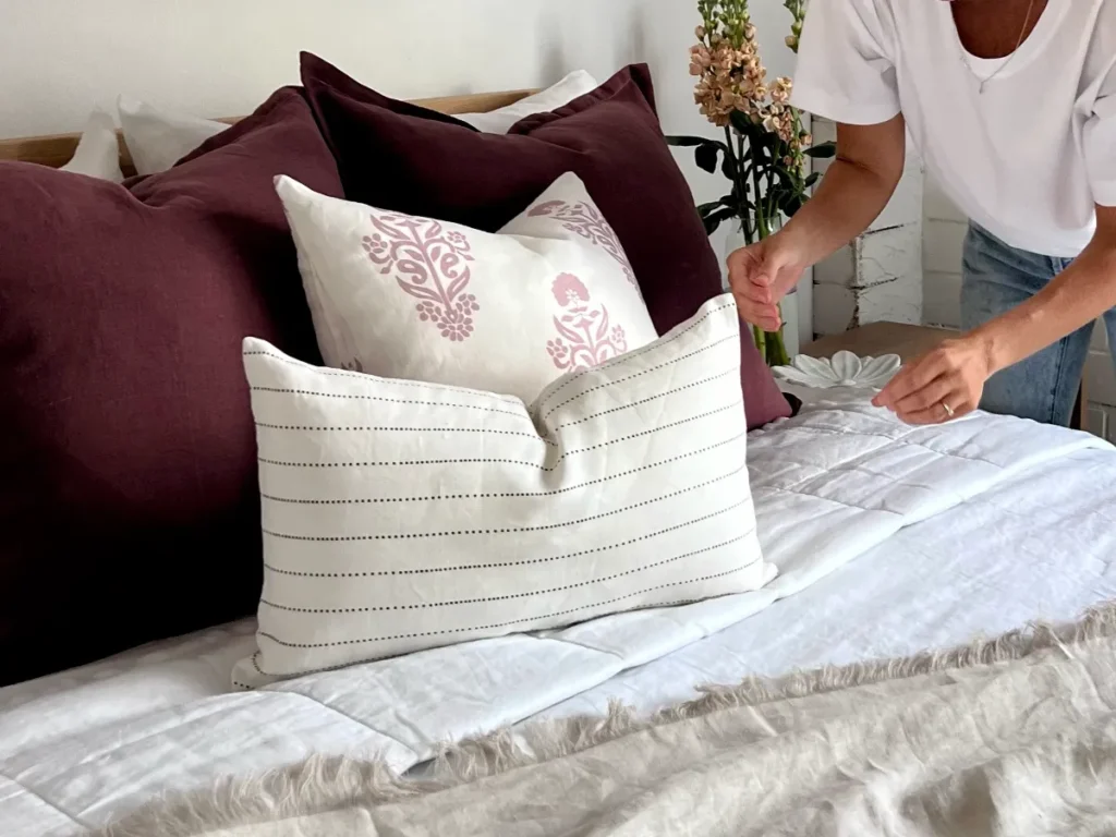 A woman is getting started with cushions by arranging them on a bed.