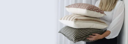 A woman is leaning against a wall with designer cushions in different styles in her hands.