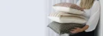 A woman is leaning against a wall with designer cushions in different styles in her hands.
