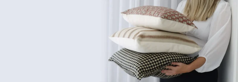 A woman is leaning against a wall with designer cushions in different styles in her hands.