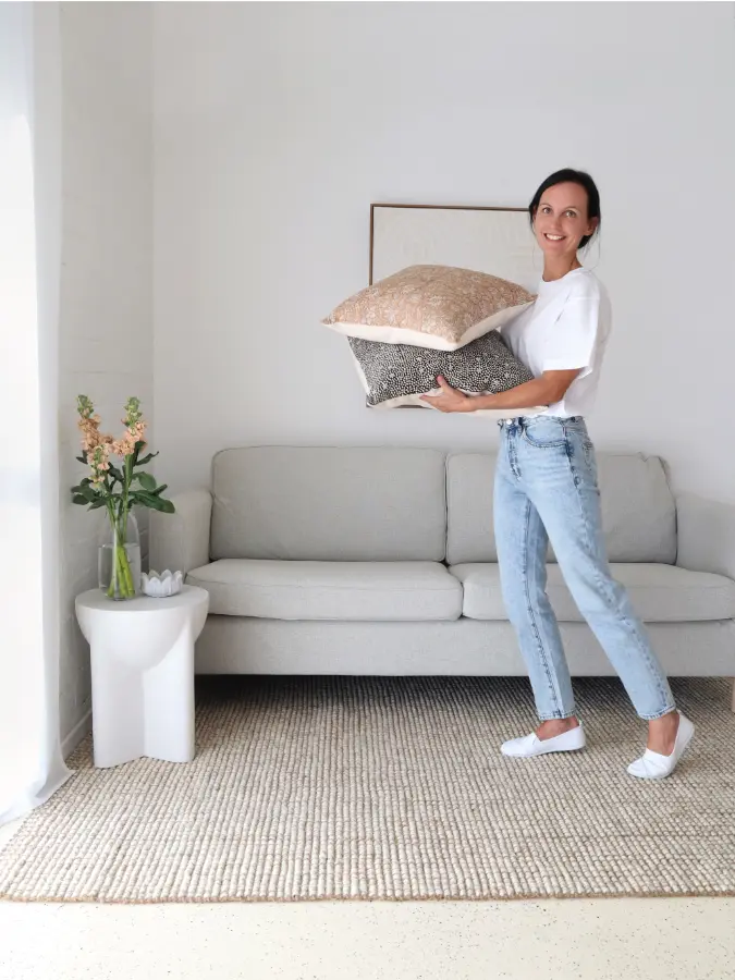 A woman is smiling and standing while holding two cushion covers.