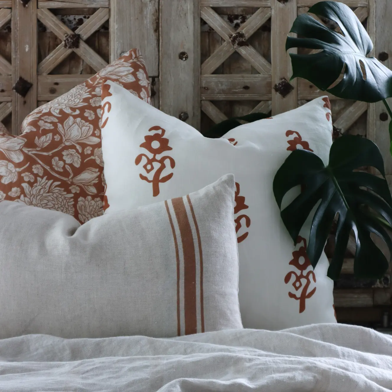 A wood background with a collection of cushions in similar colours styled with greenery nearby.