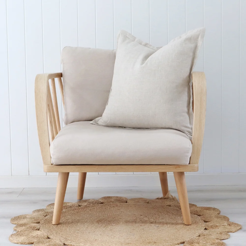 A wooden armchair with a natural cushion placed off centre.
