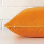 A yellow cushion arranged sideways in front of a wall. The large size and velvet fabric are shown and the seams are clearly visible.