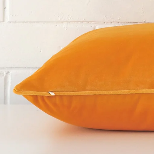 A yellow cushion arranged sideways in front of a wall. The large size and velvet fabric are shown and the seams are clearly visible.